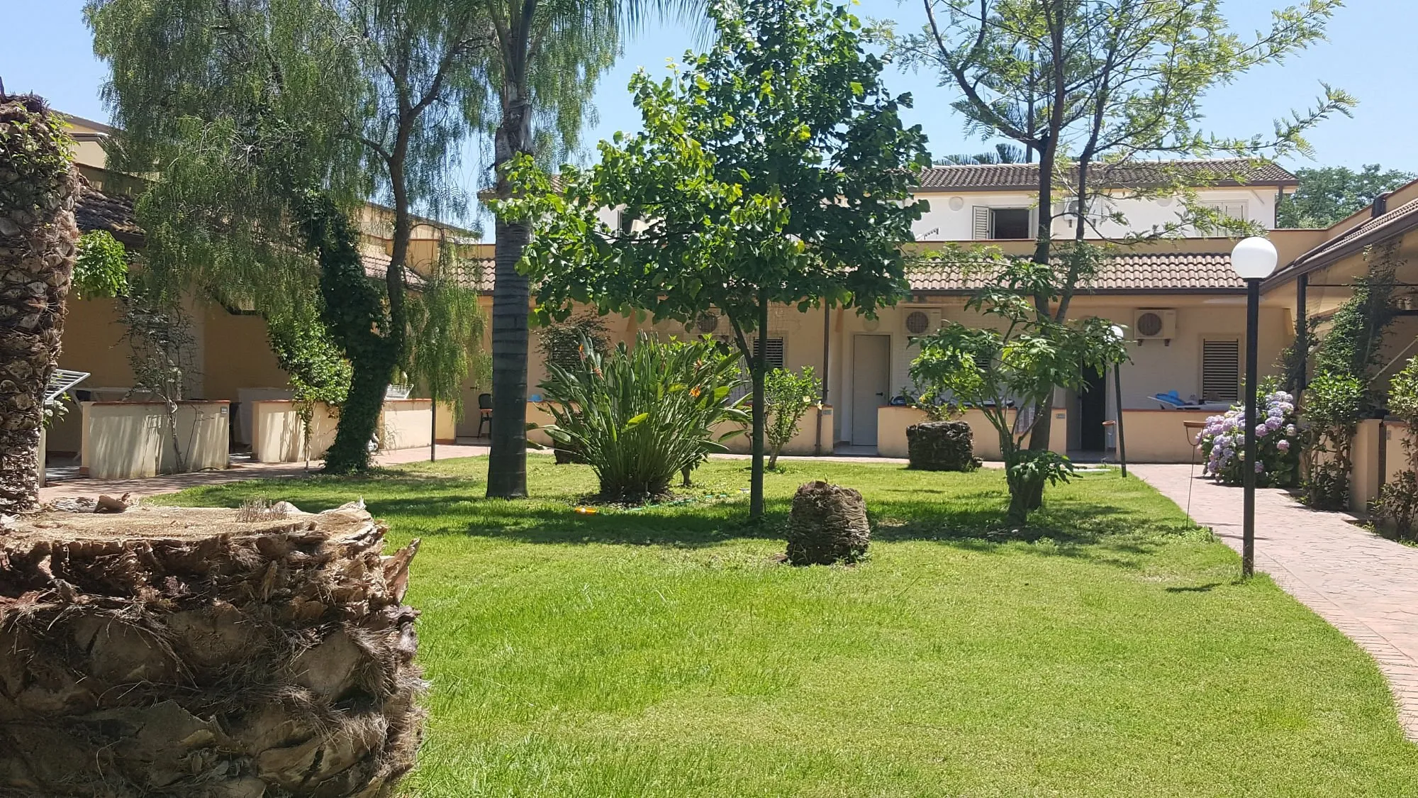 Giardino verde curato con prato, alberi e bungalow gialli del residence