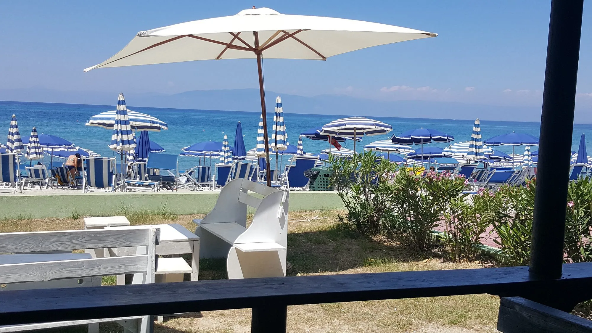 Vista sul mare dalla spiaggia con ombrelloni a righe blu e lettini