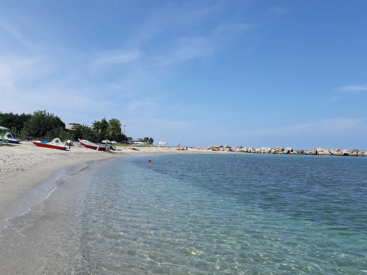 Spiaggia di sabbia con mare cristallino, pedalò e scogliera frangiflutti