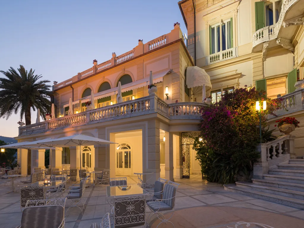 Terrazza esterna dell'hotel al tramonto con tavoli, illuminazione calda e architettura storica