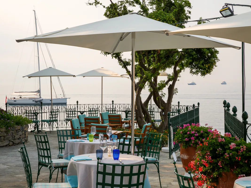 Terrazza ristorante sul mare al tramonto con tavoli apparecchiati e barche a vela all'orizzonte