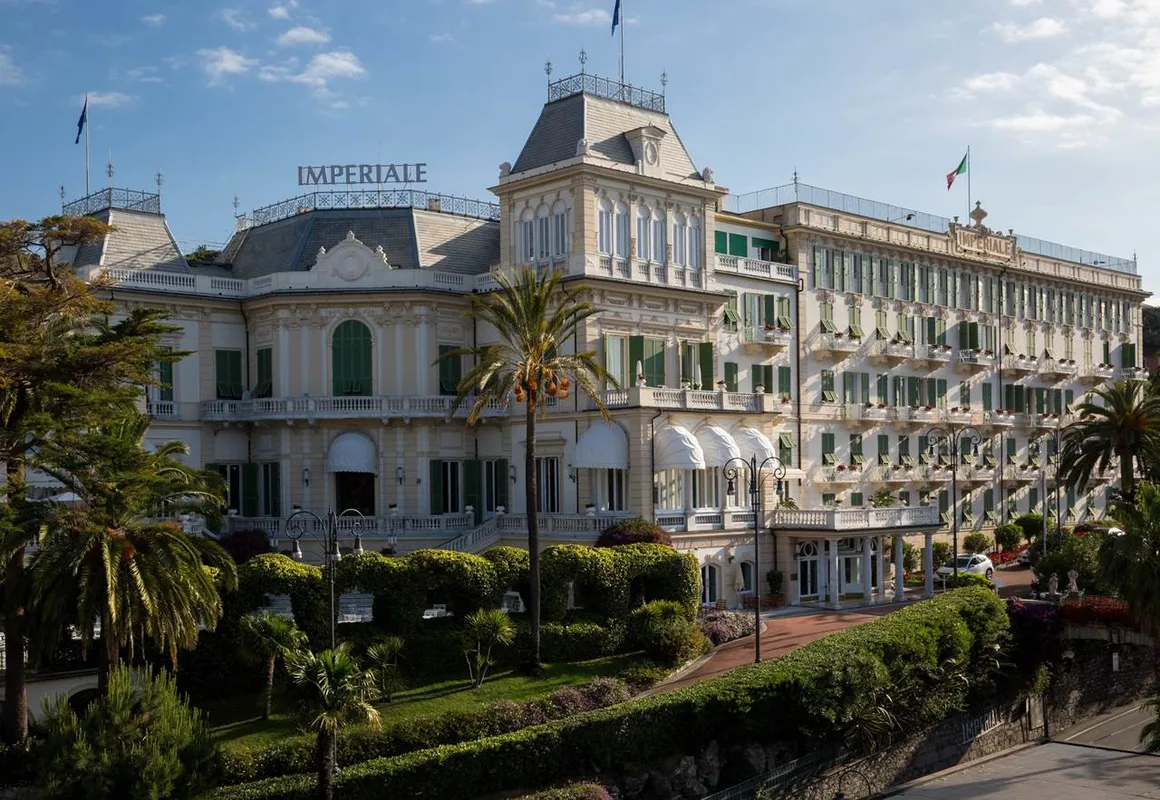 Facciata storica dell'Imperiale Palace Hotel con palme, giardini curati e cielo azzurro