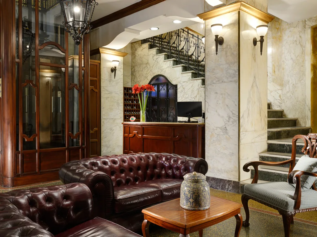 Hall dell'hotel con divani in pelle Chesterfield, reception in legno e scala in marmo
