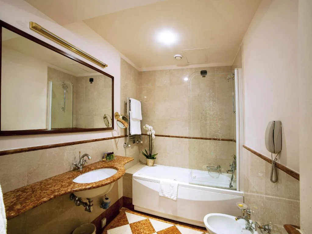 Bagno con vasca, parete in vetro, lavabo in marmo e specchio ingranditore
