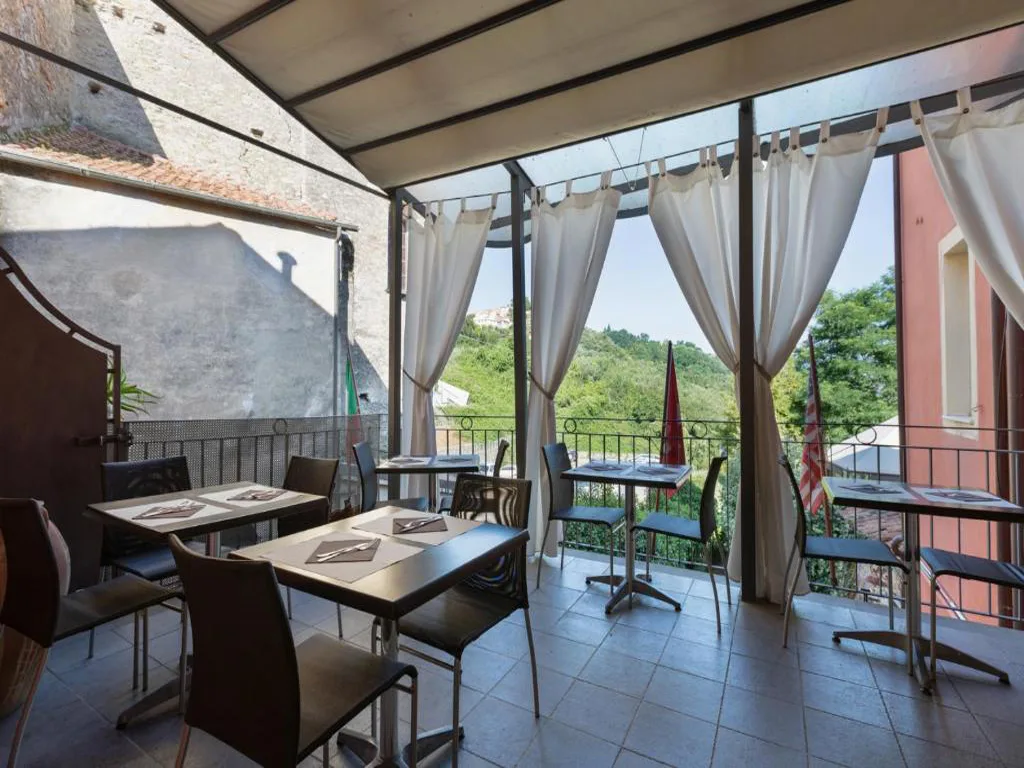 Terrazza ristorante con tavoli apparecchiati, tende bianche e vista sulla collina