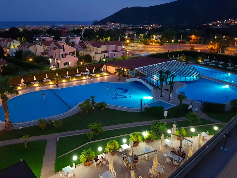 Vista notturna delle piscine illuminate del resort con vista sul mare