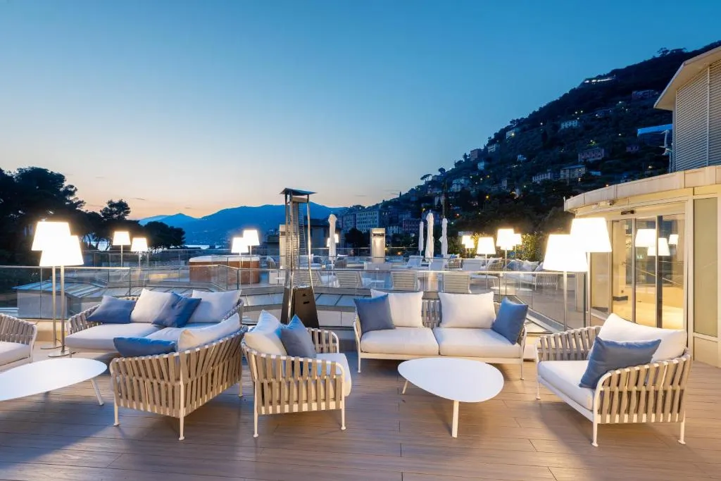 Terrazza panoramica al tramonto con divani imbottiti, lampade e vista sulle colline e sul mare
