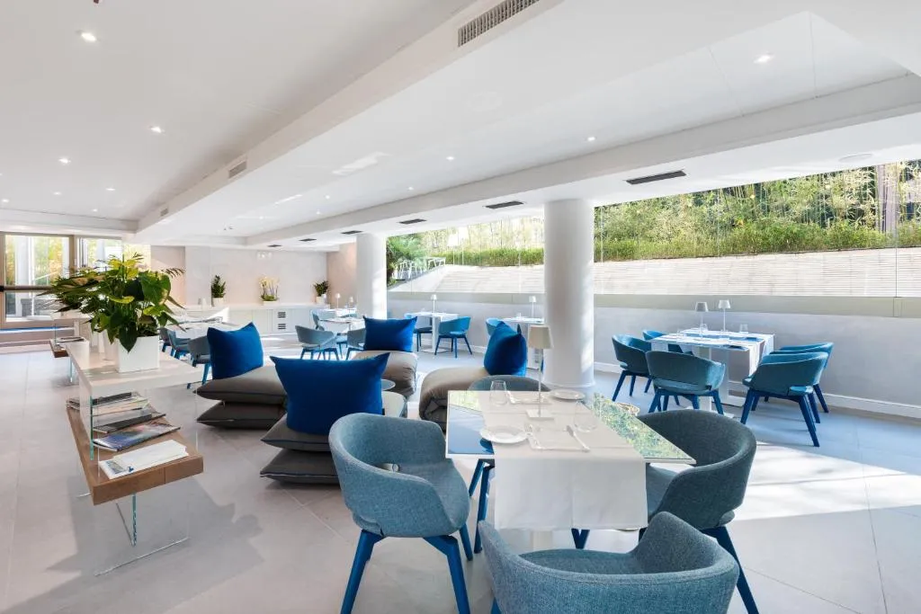 Sala ristorante luminosa con sedute blu, tavoli apparecchiati e ampie vetrate sul verde