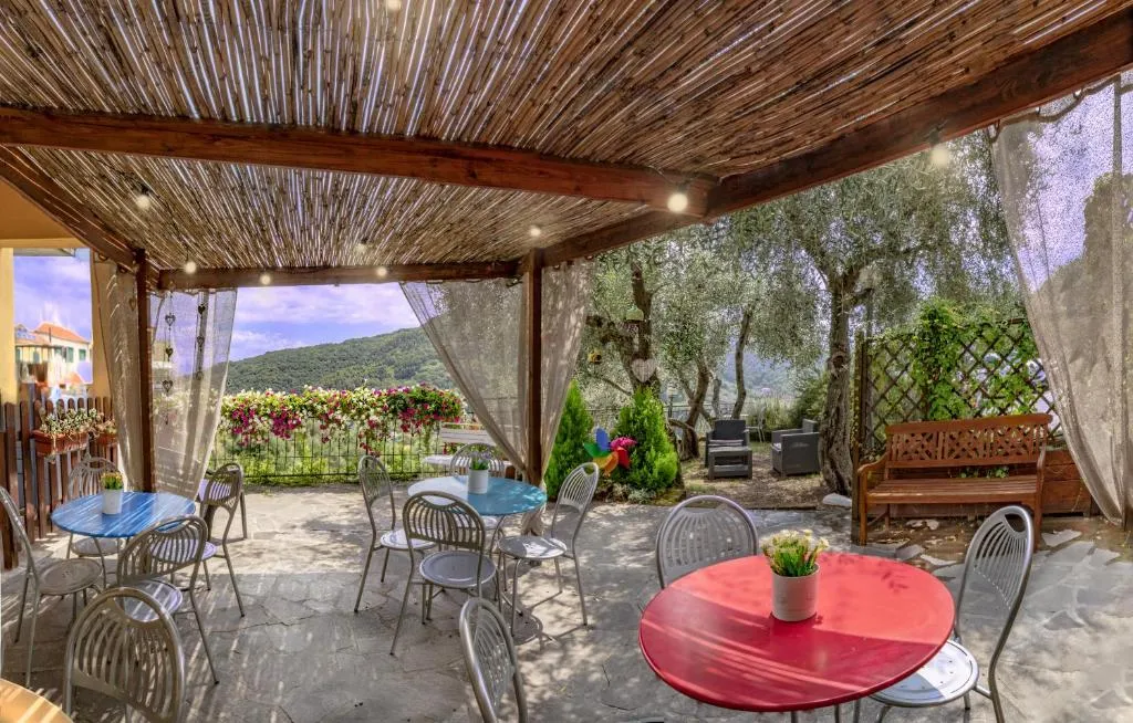 Area pranzo all'aperto sotto pergolato in canne con tavoli colorati e vista panoramica