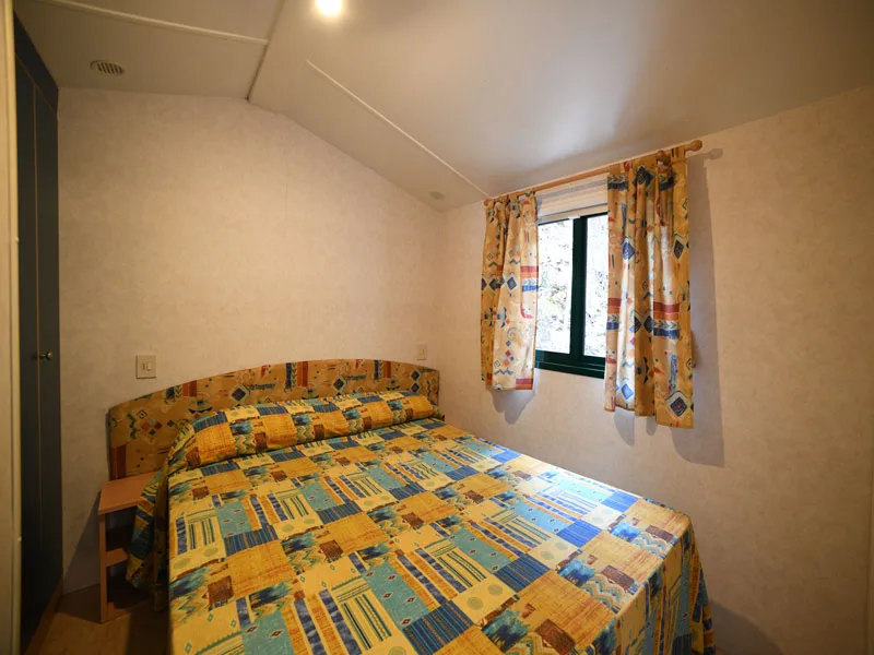 Camera matrimoniale con letto dai motivi colorati e finestra con tende