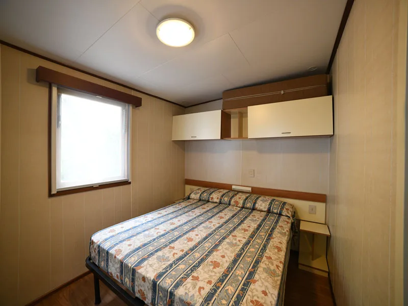 Camera matrimoniale con letto a righe, pensili e finestra luminosa