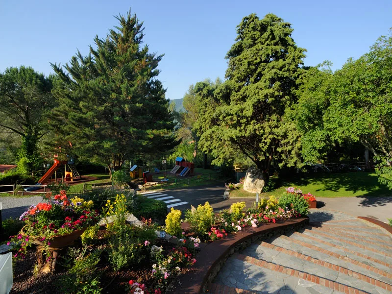 Giardino con area giochi per bambini, aiuole fiorite e grandi alberi