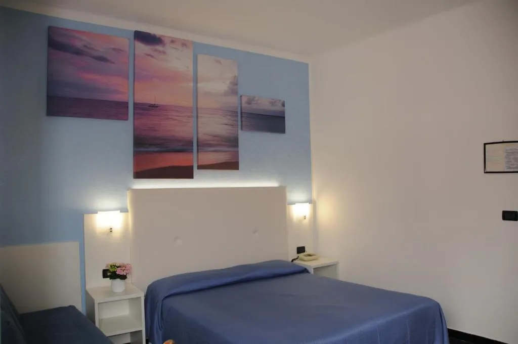 Camera matrimoniale con copriletto blu, parete azzurra con quadri di tramonto sul mare e comodini bianchi