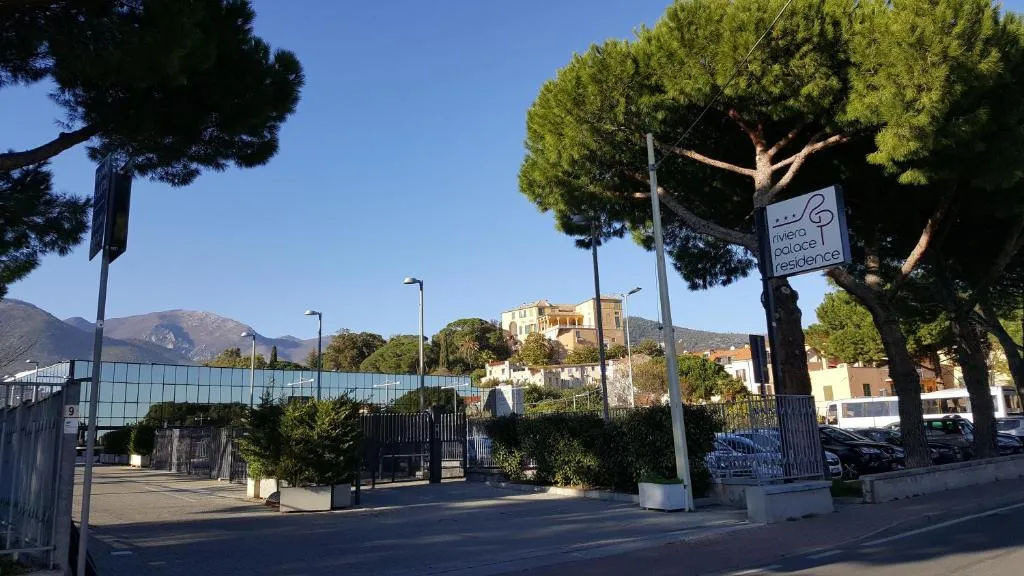 Ingresso esterno del Riviera Palace Residence con insegna, pini marittimi e colline