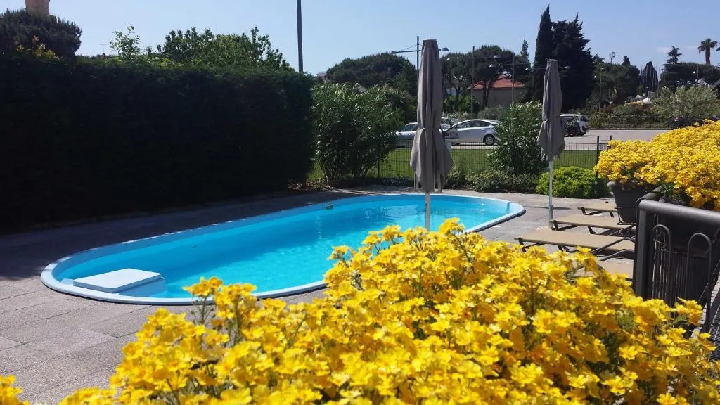 Piscina ovale circondata da fiori gialli, ombrelloni chiusi e siepe