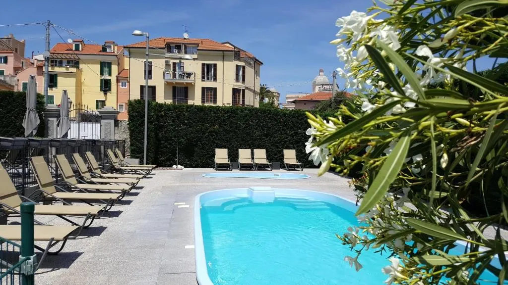 Piscina con lettini abbronzanti, oleandri in fiore e palazzi colorati sullo sfondo