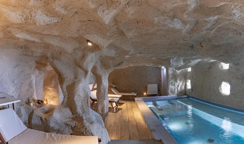Piscina interna in stile grotta con pareti di roccia e lettini relax