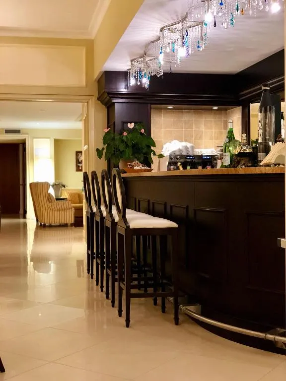 Bar dell'hotel con bancone in legno scuro, sgabelli eleganti e lampadario decorativo