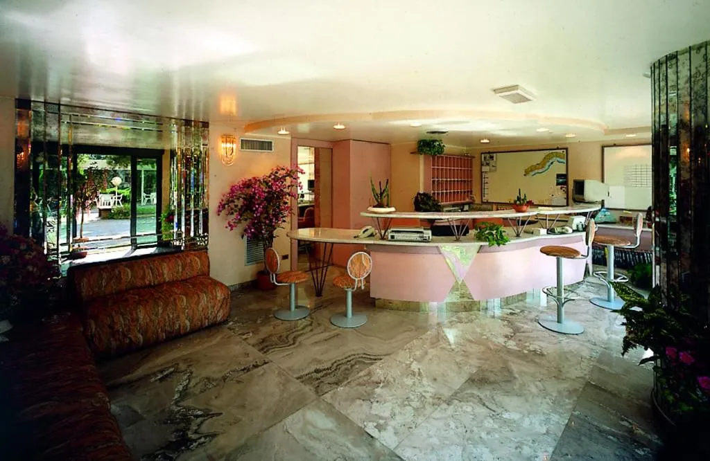 Hall dell'hotel con reception rosa, sgabelli, divano e ampie vetrate sul giardino