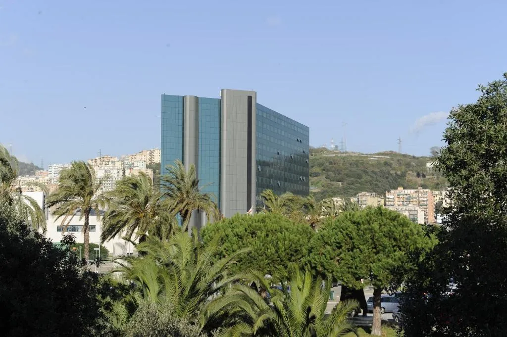 Vista esterna dell'hotel, edificio moderno in vetro circondato da palme e colline