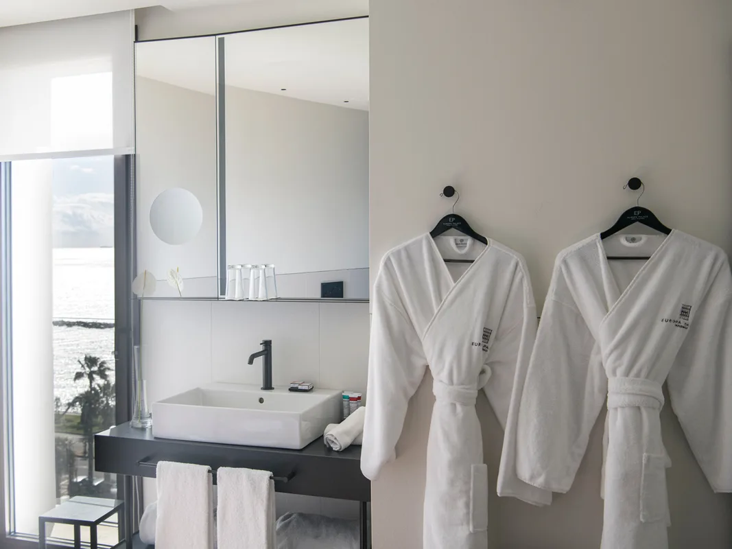 Bagno luminoso con lavabo nero, specchio e due accappatoi bianchi appesi, vista mare dalla finestra