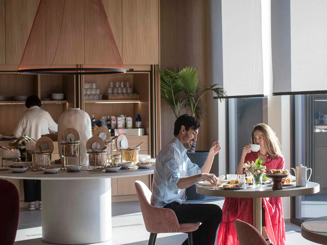 Sala colazioni con buffet e coppia seduta a un tavolo che gusta caffè e pasticceria