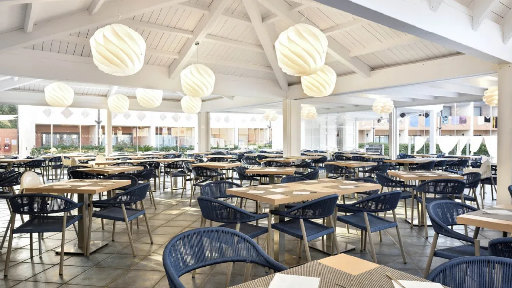 Sala ristorante con tavoli in legno e sedie blu sotto tetto in legno bianco