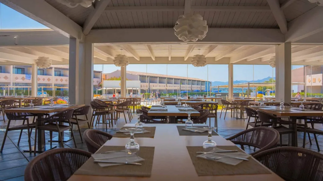 Sala ristorante con tavoli apparecchiati e vista sul resort al tramonto