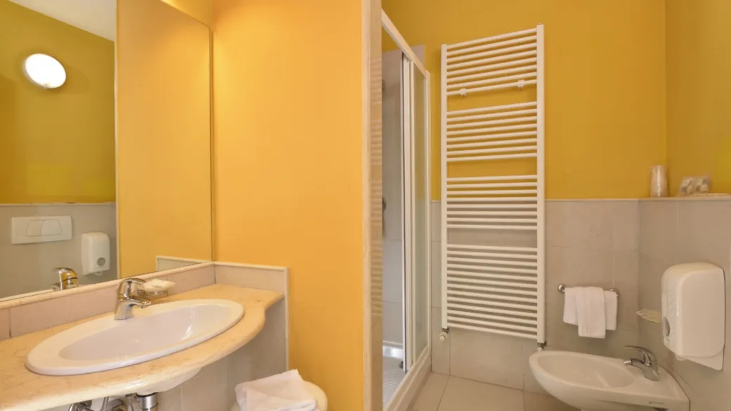 Bagno della camera con lavabo, specchio, doccia e pareti gialle