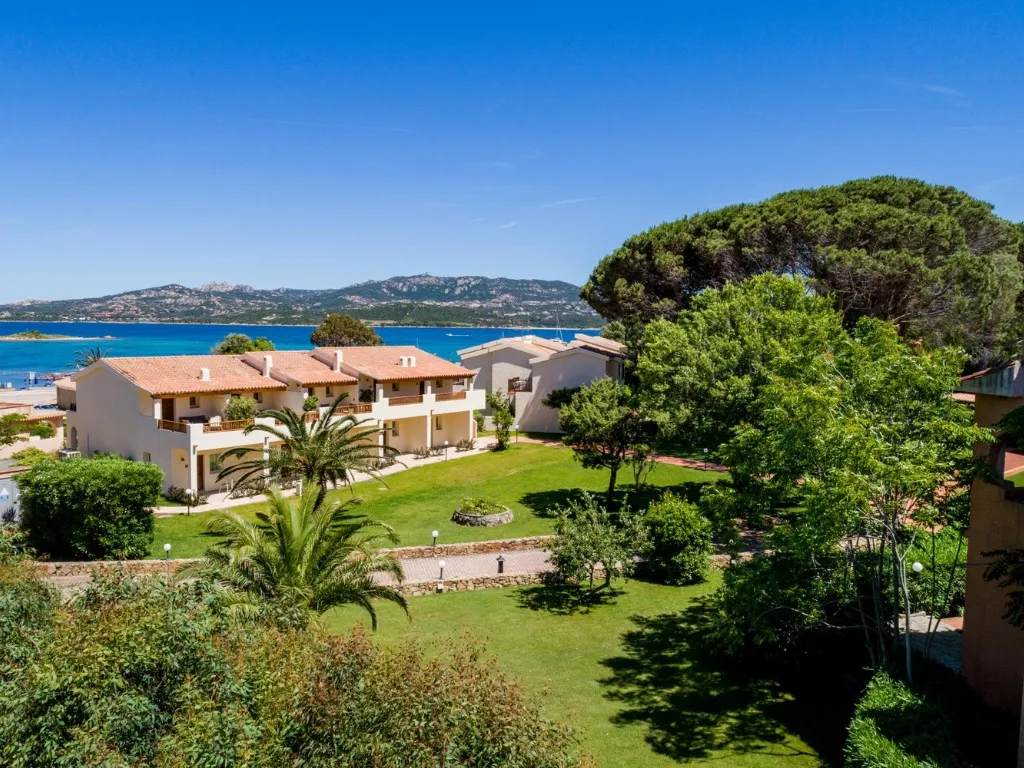 Giardino verde del resort con palme, edifici bianchi e vista mare