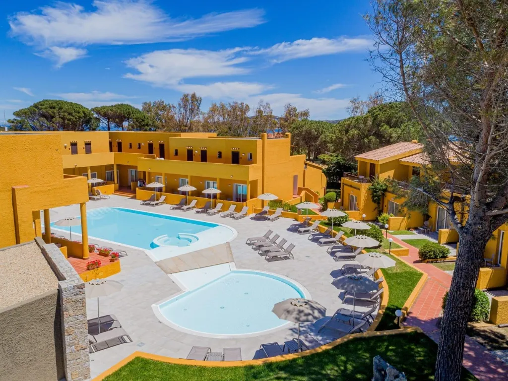 Piscina con lettini e ombrelloni circondata da edifici gialli del resort