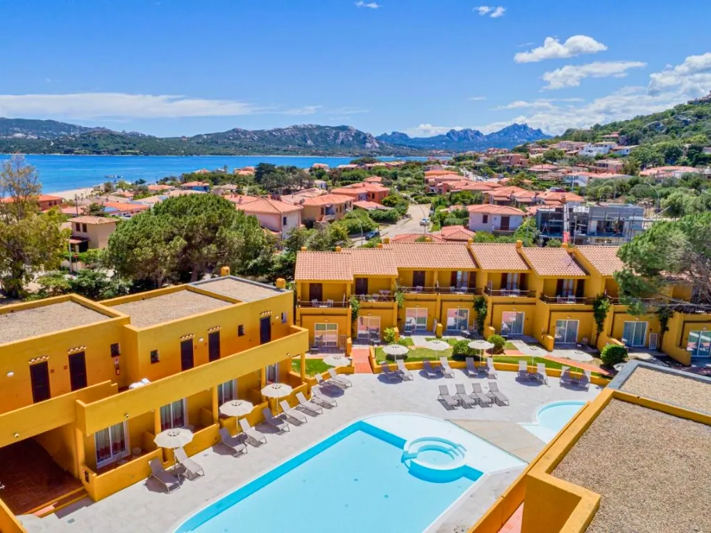 Vista panoramica del resort con piscina, ombrelloni e mare azzurro all'orizzonte