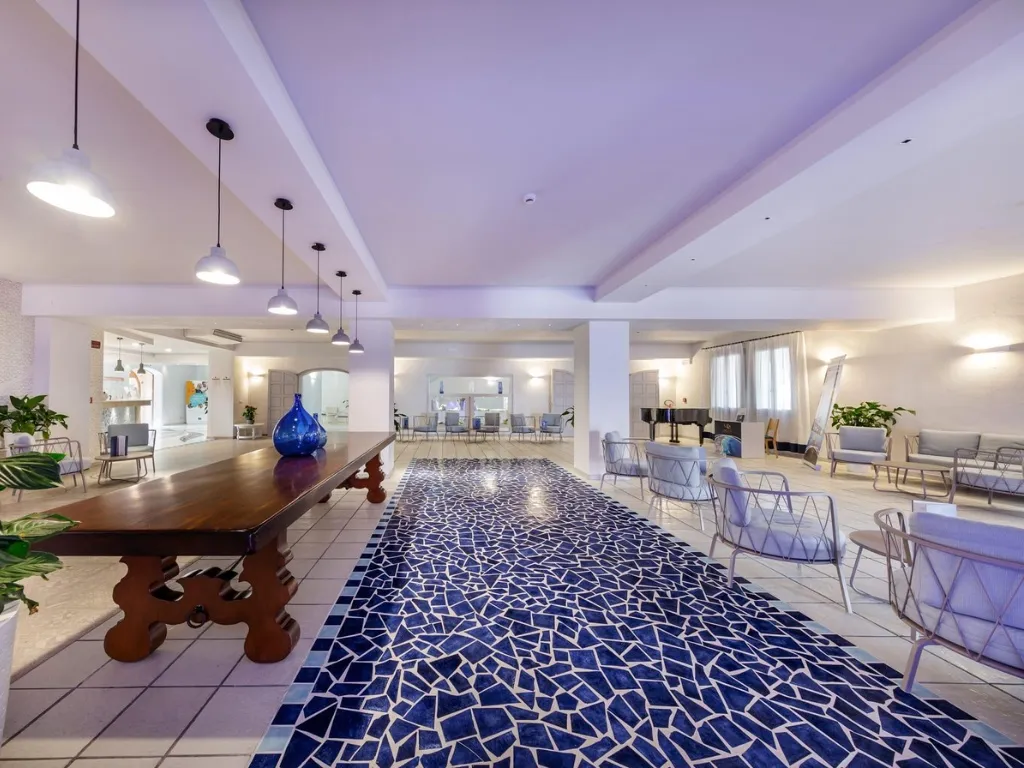 Ampia hall dell'hotel con tappeto a mosaico blu, poltrone e tavolo in legno