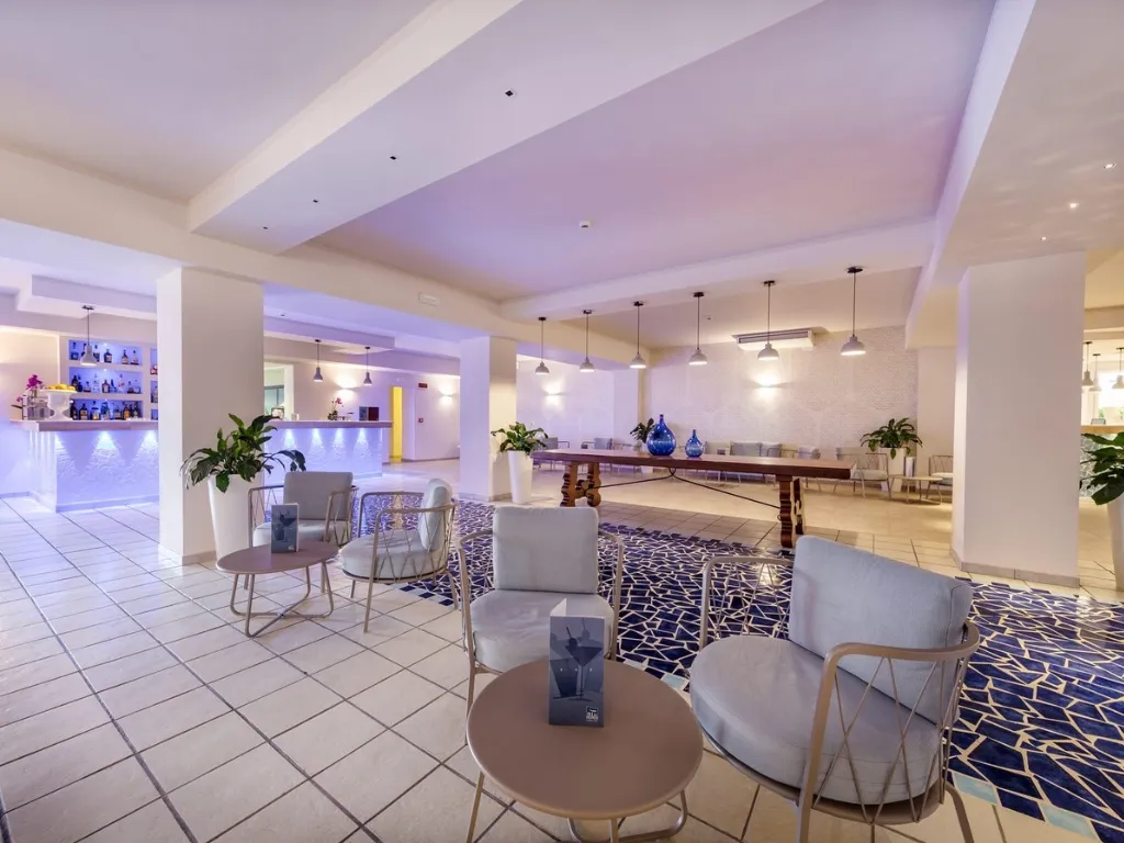 Area lounge dell'hotel con poltrone, tavolini e bar sullo sfondo