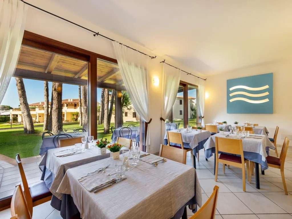 Ristorante con tavoli eleganti e grandi vetrate affacciate sul giardino con pini
