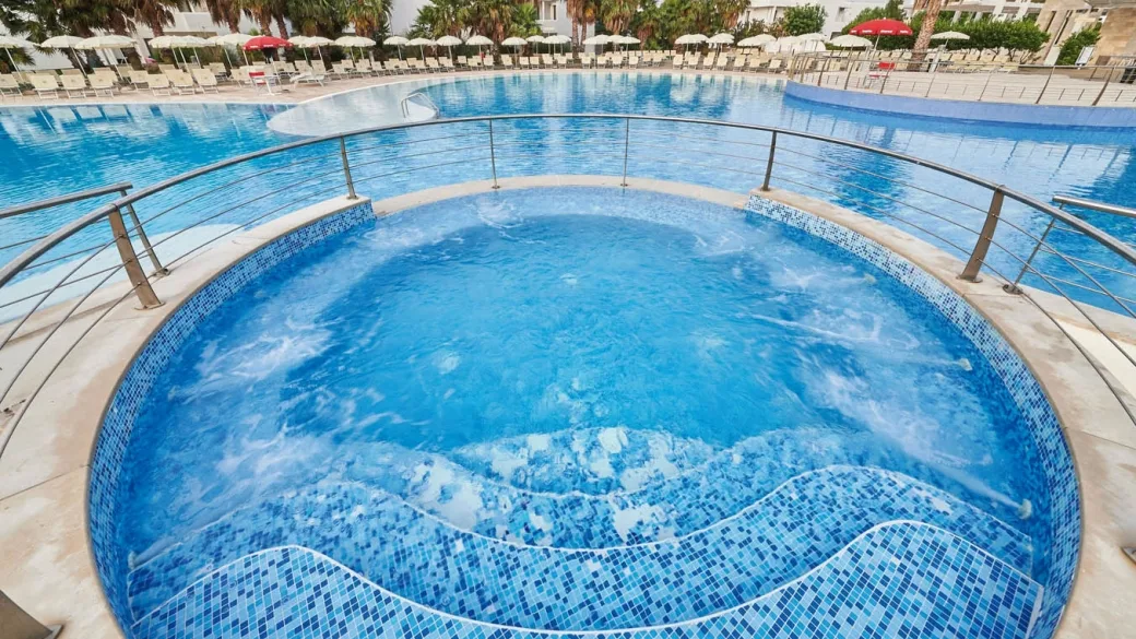 Vasca idromassaggio circolare con mosaico blu collegata alla grande piscina