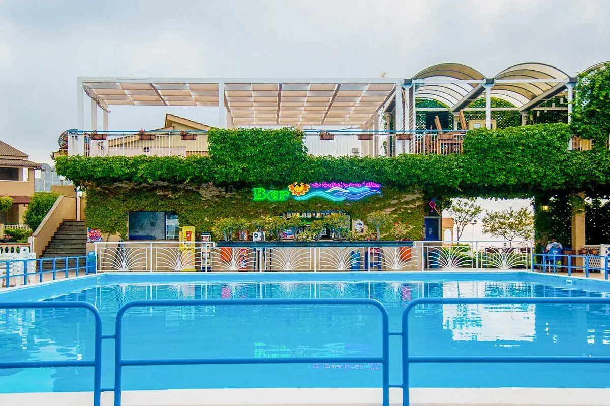 Bar a bordo piscina con pergolato bianco e parete ricoperta di edera