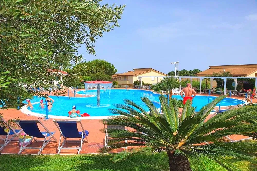 Piscina con fontana centrale e lettini, palme e giardini verdi attorno