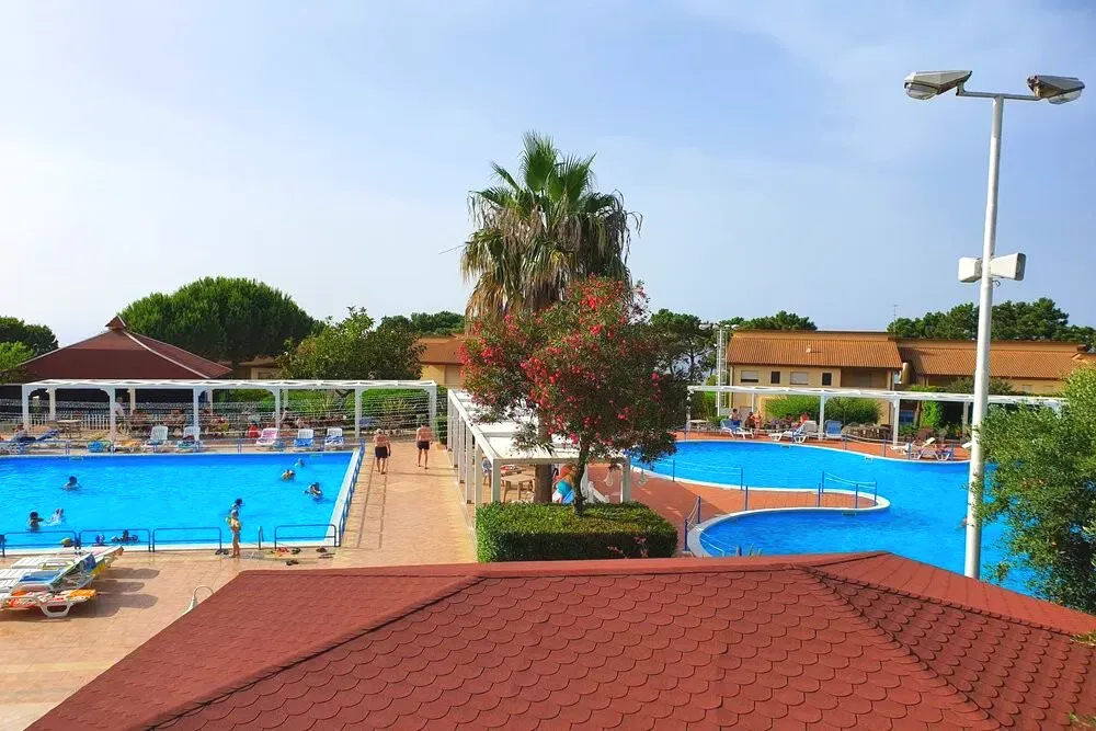 Due piscine con lettini, palme e alberi fioriti viste dall'alto del resort