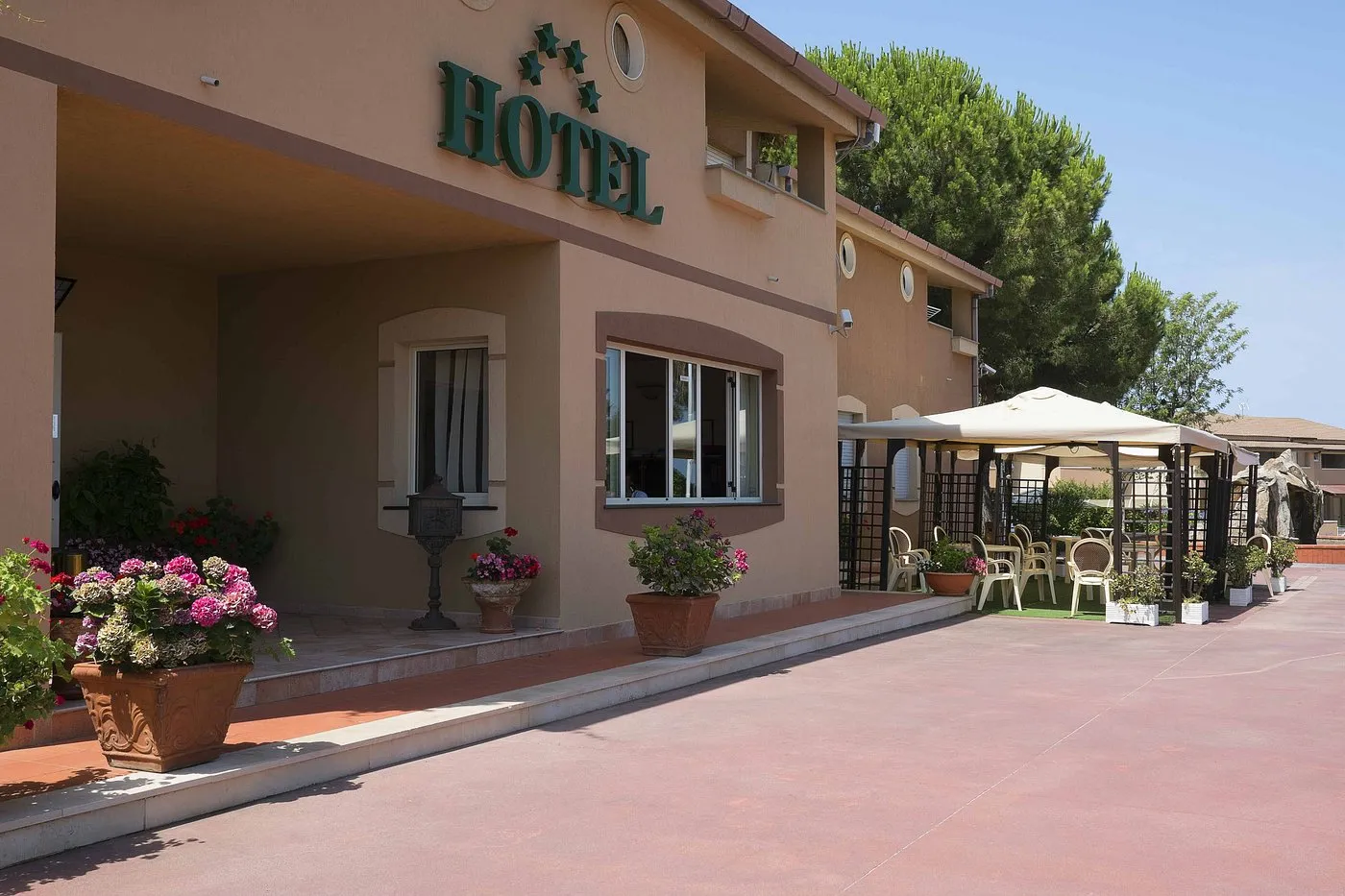 Ingresso dell'hotel con insegna, fiori colorati e area esterna con gazebo