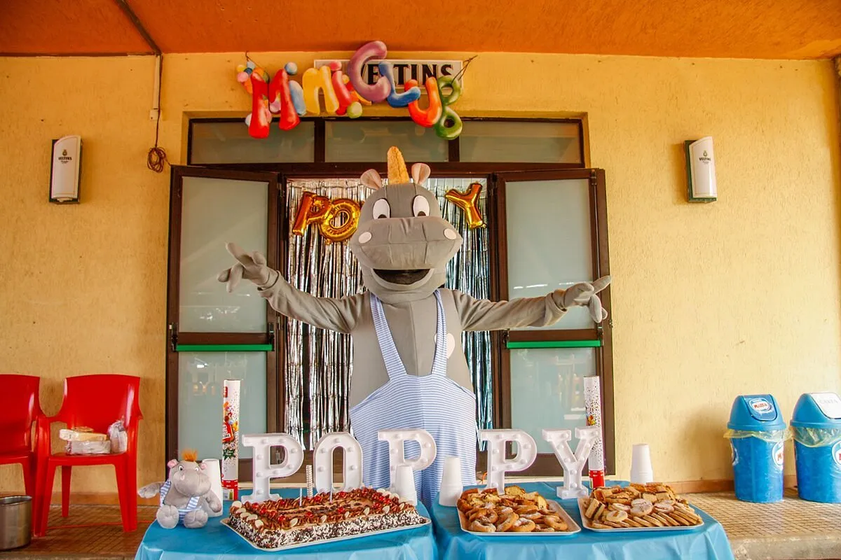 Mascotte Poppy del mini club con tavolo di dolci e festoni colorati