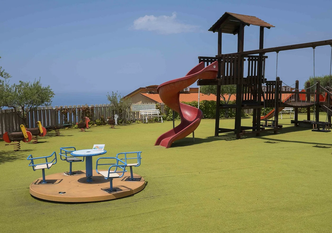 Area giochi per bambini con scivolo, giostrina e vista sul mare