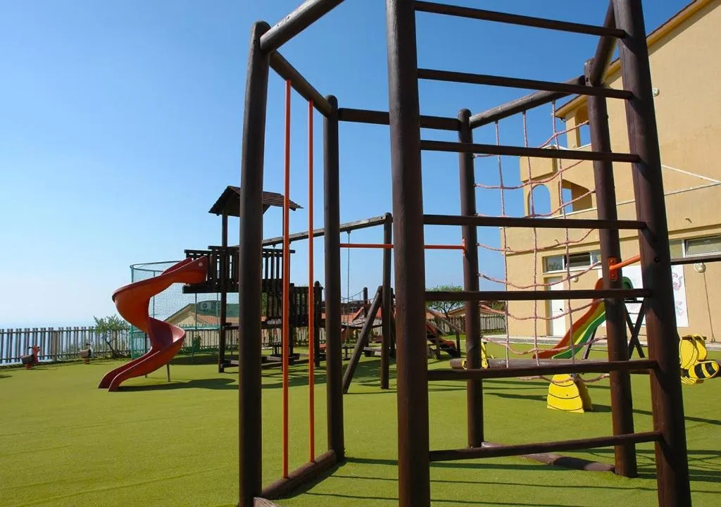 Parco giochi con strutture in legno e scivoli su prato sintetico verde