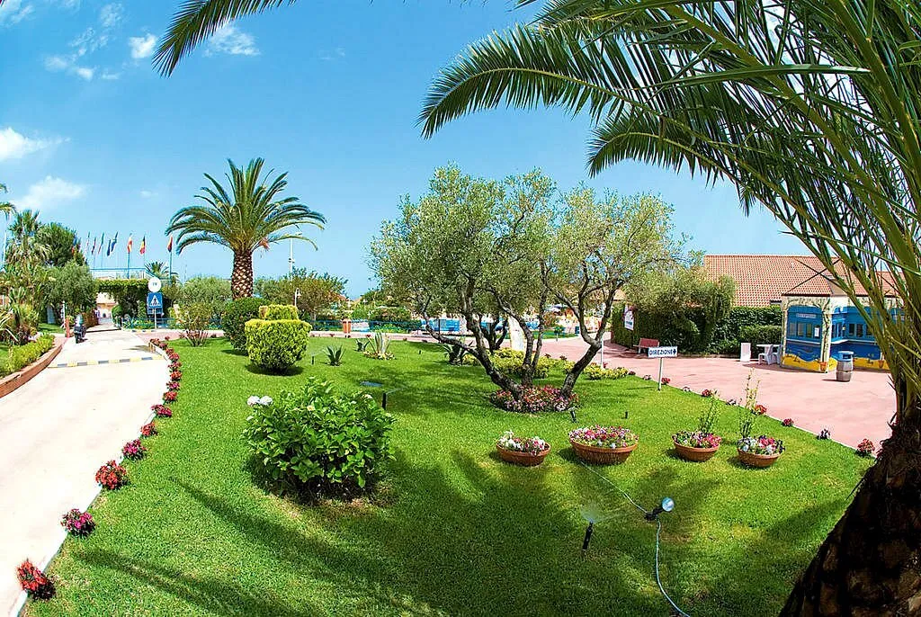 Giardino curato del resort con prato verde, palme, fiori e vialetto d'ingresso