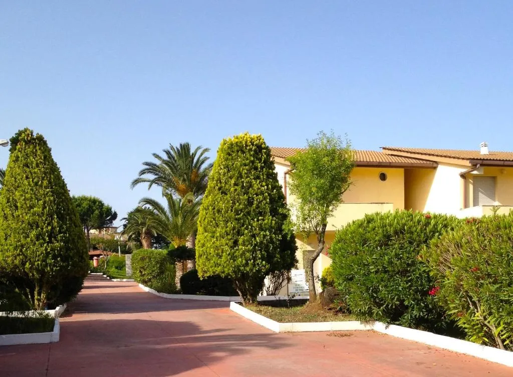 Vialetto interno del resort con siepi curate, palme e edifici gialli