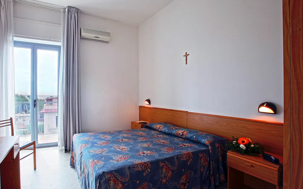 Camera con letto matrimoniale, balcone e arredi in legno chiaro